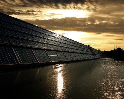 Silhouetted solar panels reflect sunset in tranquil waters, showcasing renewable energy.